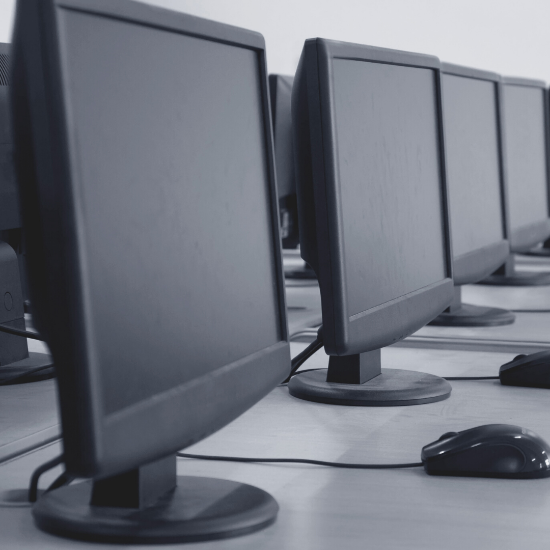 four black computer monitors and computer mice on grey desk